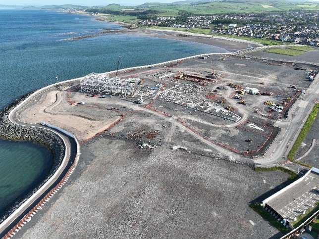 Aerial view of building site surrounded by sea and houses.