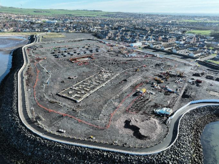 Aerial view of building site situated by the sea and surrounded by houses.