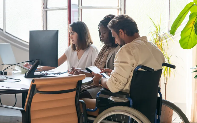 Three people sitting at a table in an office, one of them is in a wheelchair