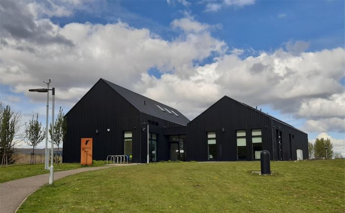 Exterior of community centre, two adjoining black buildings surrounded by grass.