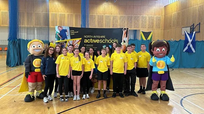 Young people and mascots standing in front of an active schools banner inside an indoor courts area