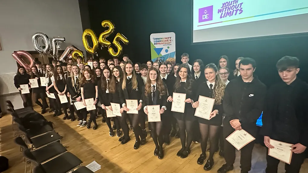 A large group of pupils in a hall holding certificates rewarding them for their hard work
