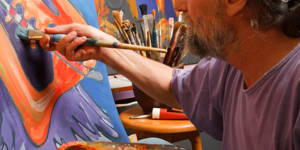 An artist paints a blue and orange picture on a canvas.