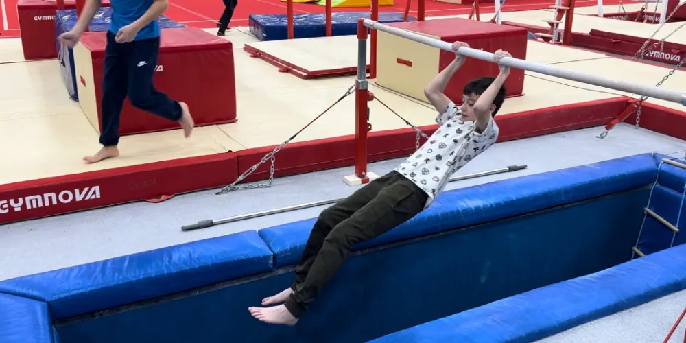 Boy swings arms from pole above gymnastics foam pit