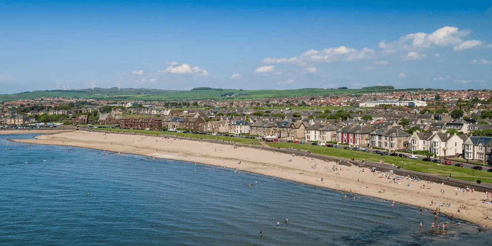 An aerial view of a beach on a sunny day with houses and hills in the background