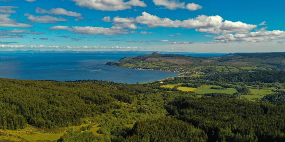 An aerial view of the coast of Arran, with rolling hillsides and blue skies