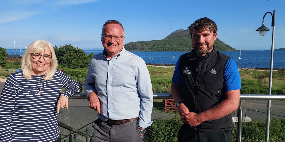 Council Leader Marie Burns and Chief Executive Craig Hatton with Martin Wood, who is Team Leader at Arran Outdoor Education Centre. A blue sky and an island are in the background