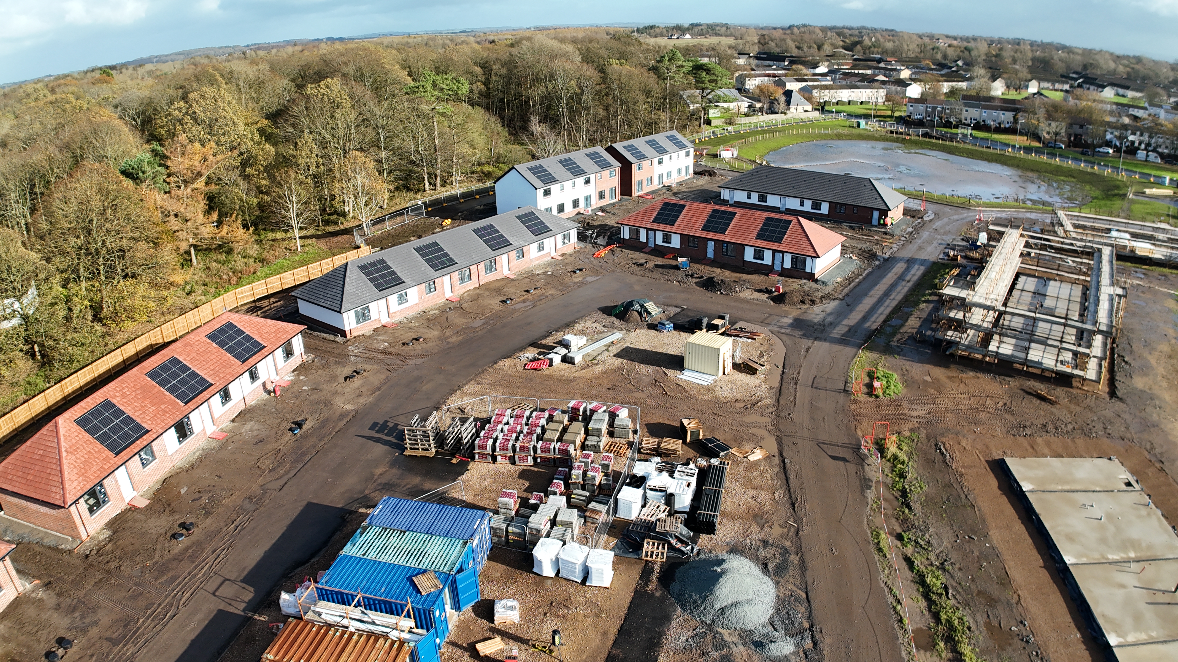 Houses being built on a new development site with trees in the background and a blue sky