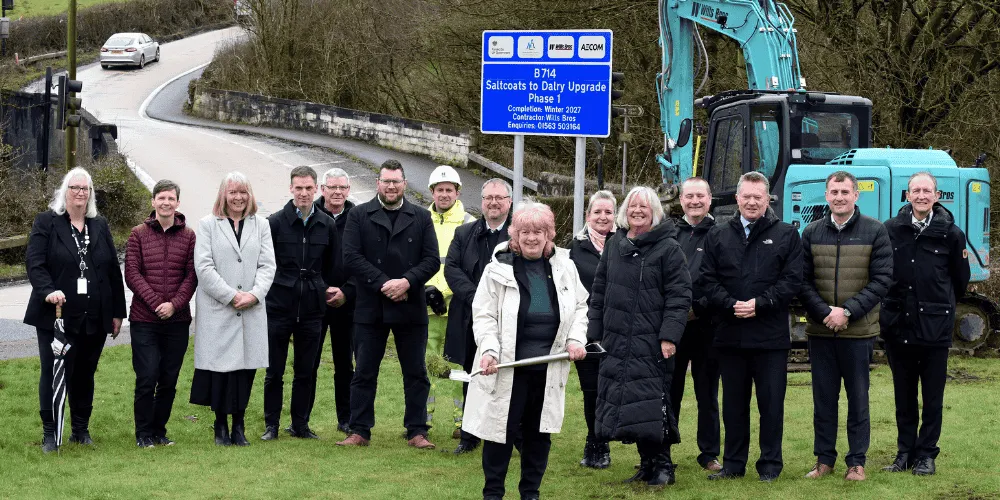 A group of 15 people standing on grass next to a road