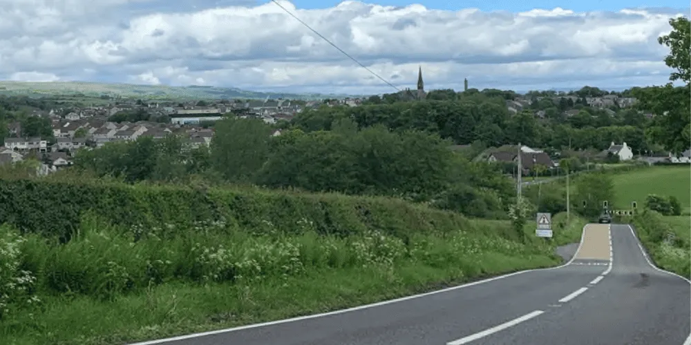 A road in a countryside setting with the skyline of a small town in the distance