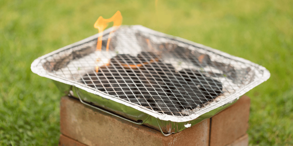 A disposable BBQ lit and resting on bricks