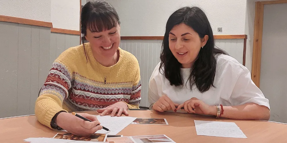 Two women sitting at a table discussing English while looking at written materials