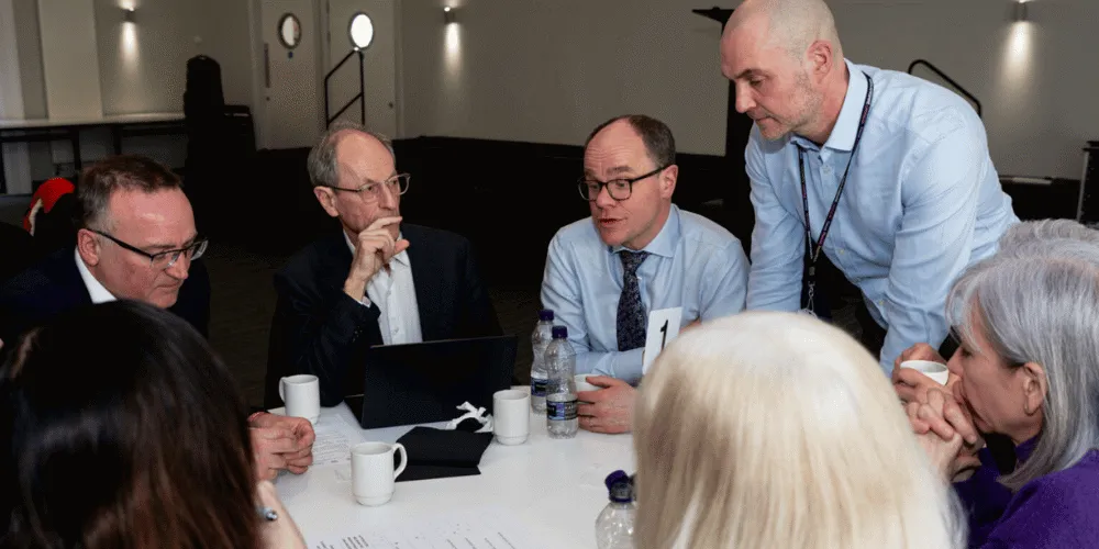 Seven men and women holding a discussion round a table.
