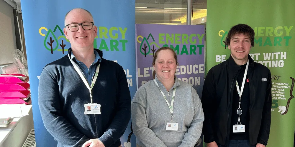 Three members of the Sustainability team in front of pop-up banners