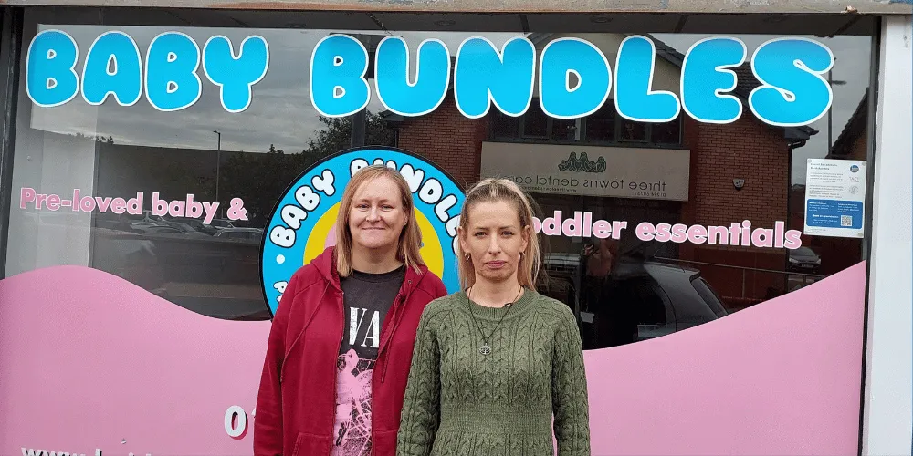 Two women standing, facing the camera, outside a baby shop