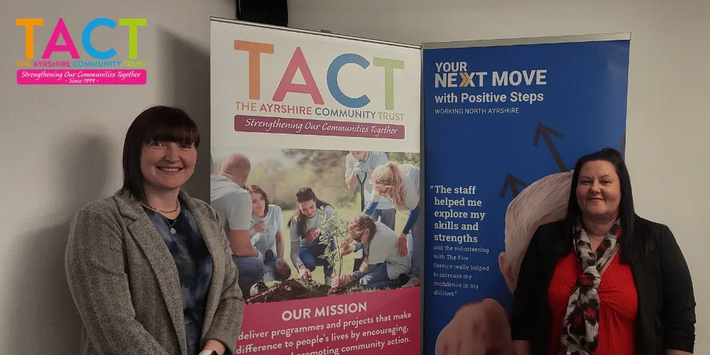 Two women standing smiling next to pop-up banners for TACT
