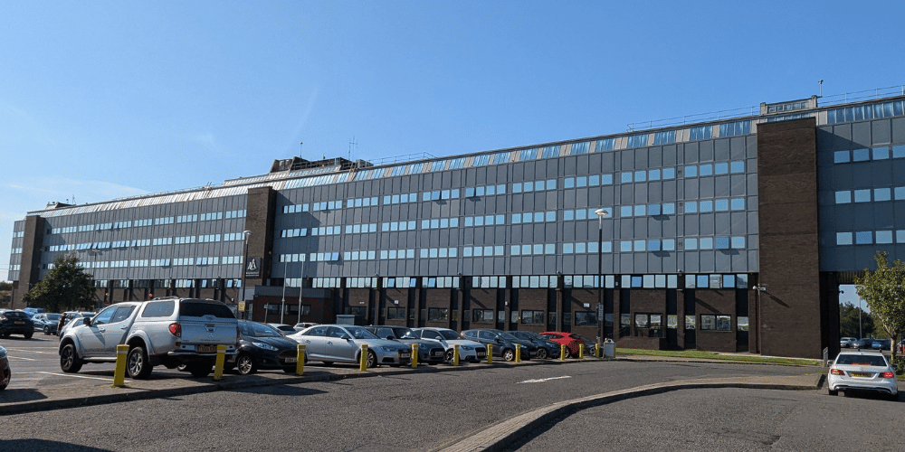 The exterior of a large building on a sunny day with cars in the foreground