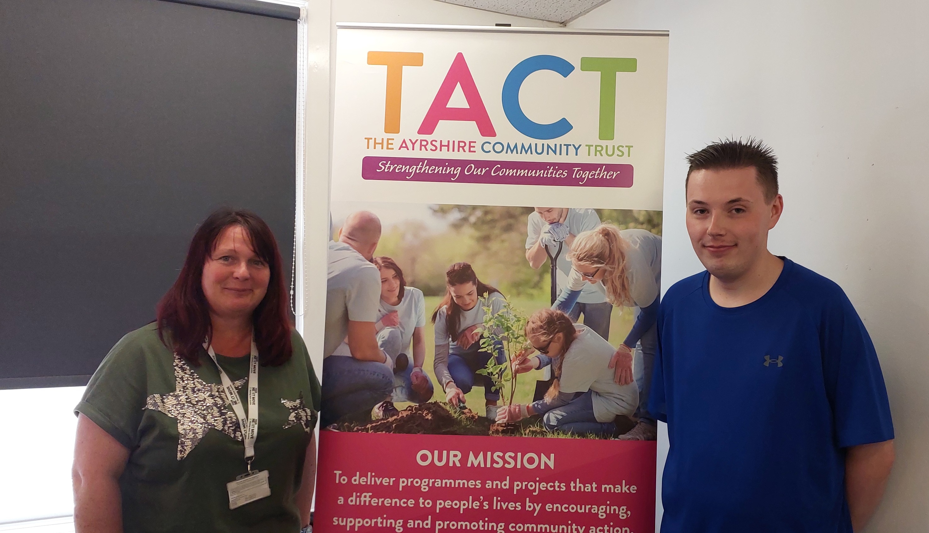 A man and a woman standing, smiling, in front of a pop-up banner
