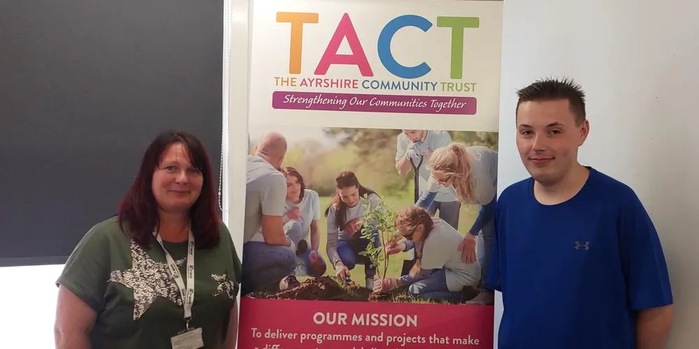 A man and a woman standing, smiling, in front of a pop-up banner
