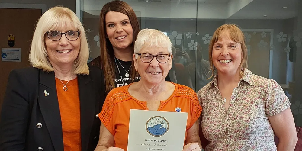 Four women smiling while one holds a certificate