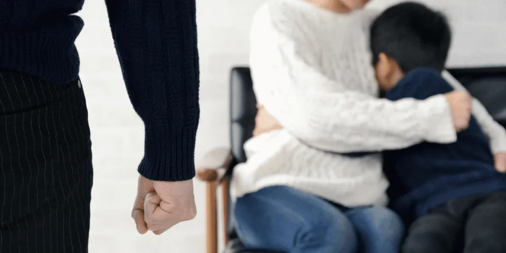 An image of a woman holding a child while a man stands near with a clenched fist