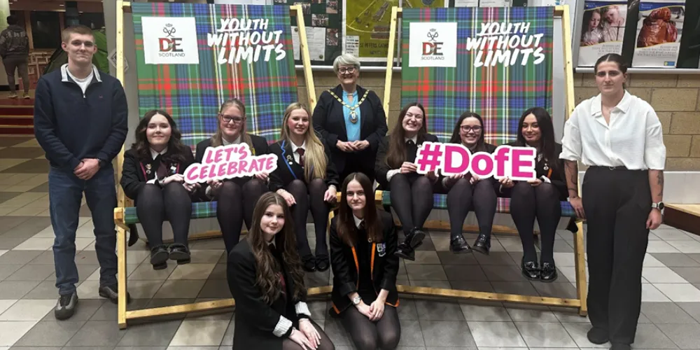 A group of adults and children in school uniform sitting on giant deck chairs