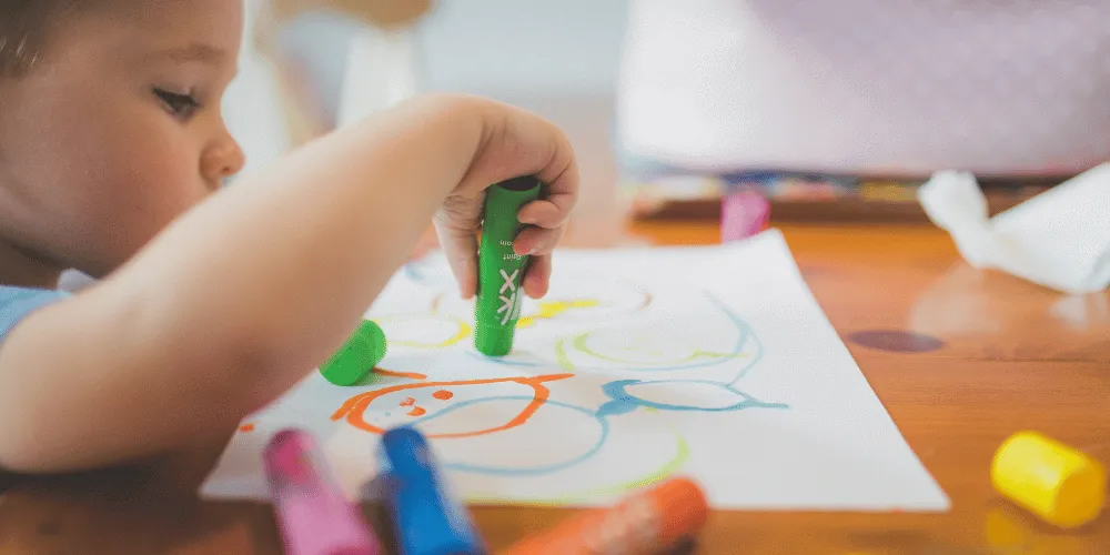 A young child using a coloured pen to draw shapes on a piece of paper