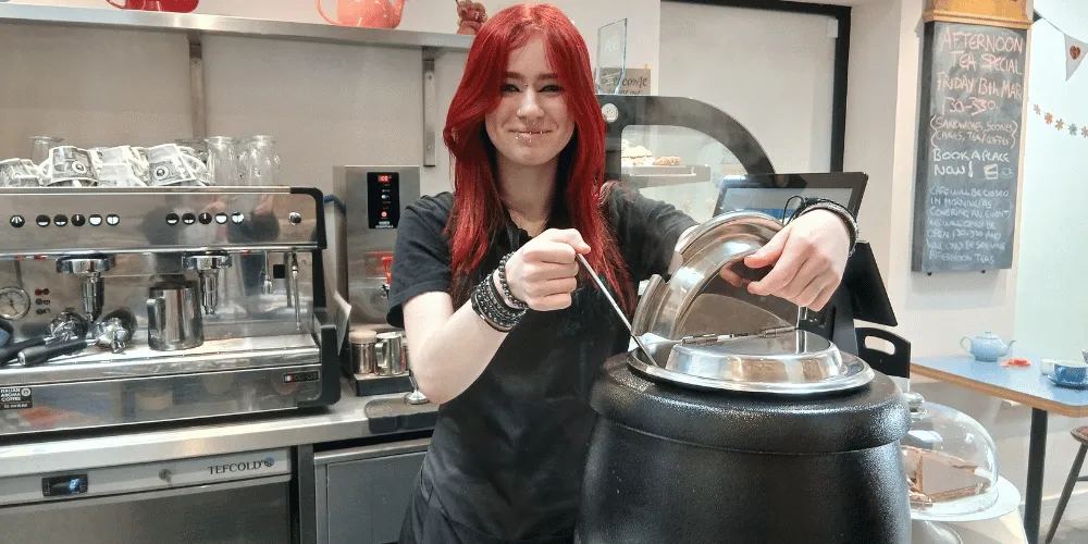 A young woman smiling at the camera while ladling soup from a soup kettle