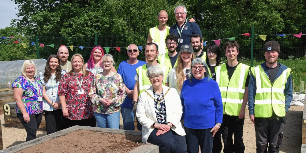 Three rows of people standing smiling at the camera, near some raised beds, with bunting strung up behind them