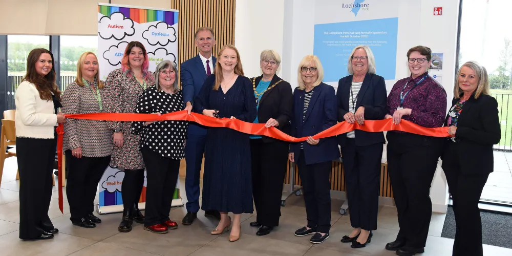 A group of people standing cutting a red ribbon