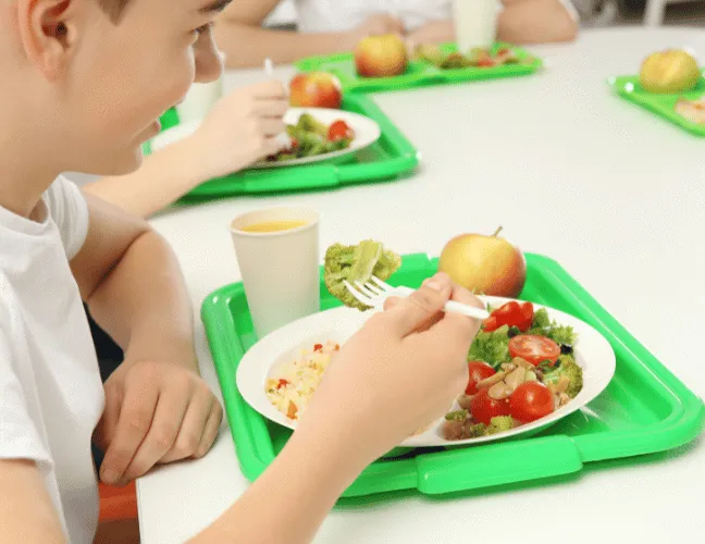 A child eating a school meal on a bright, green tray