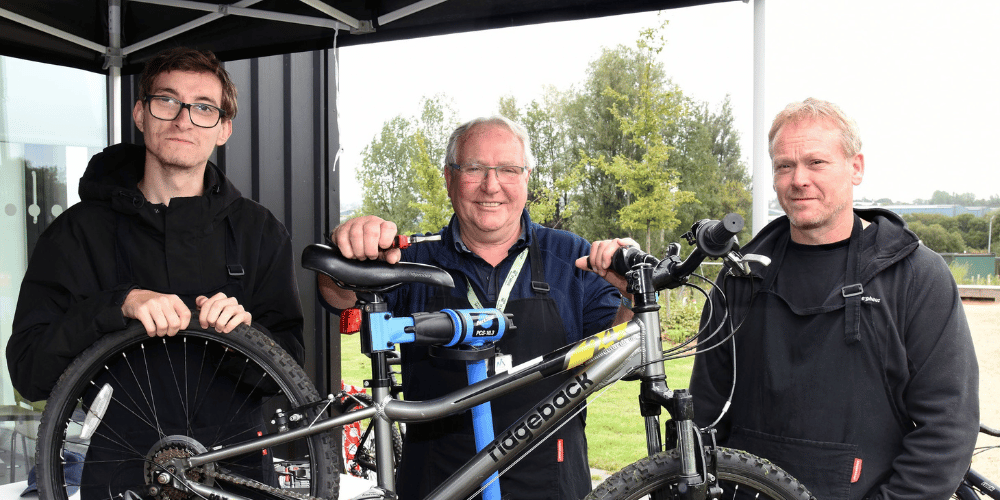 Three men, with a bike on a bike repair stand, smiling at the camera.
