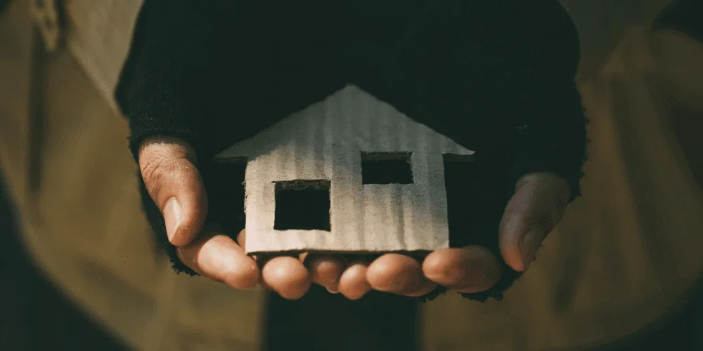 A pair of gloved hands hold a miniature representation of a house