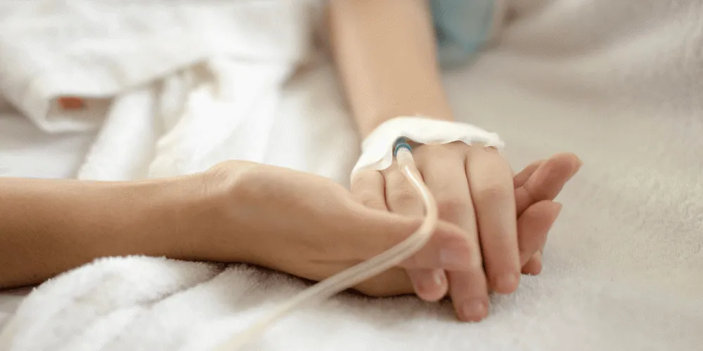 An image of two hands holding each other, one with a medical tube in the back of the hand