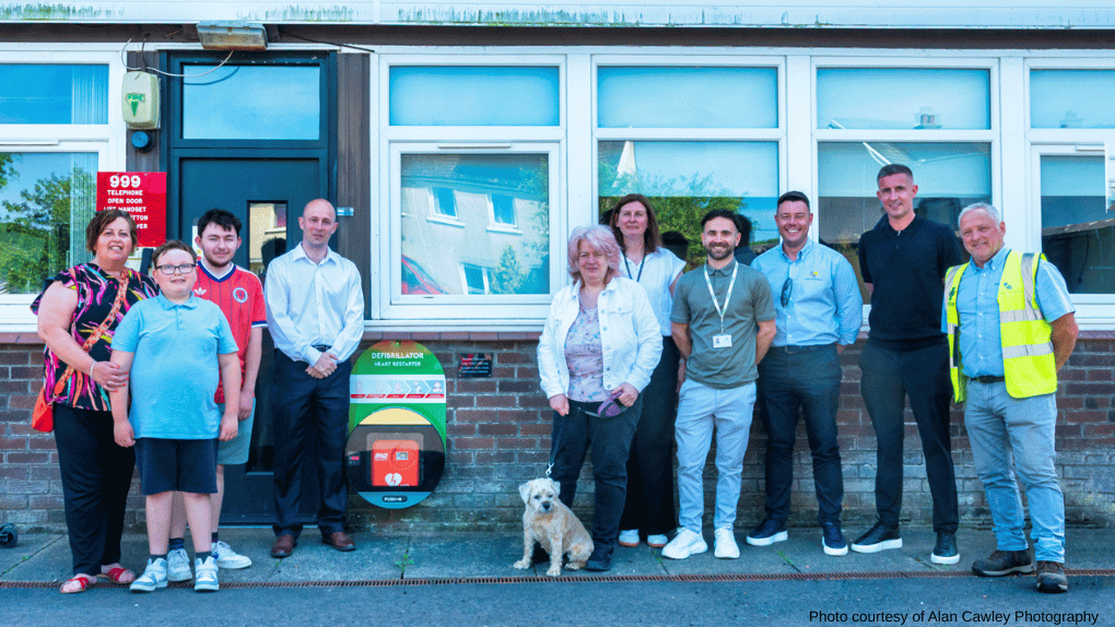 Ten people standing in a row near a defibrillator - one woman has a dog on a lead