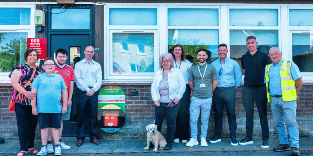 Ten people standing in a row near a defibrillator - one woman has a dog on a lead