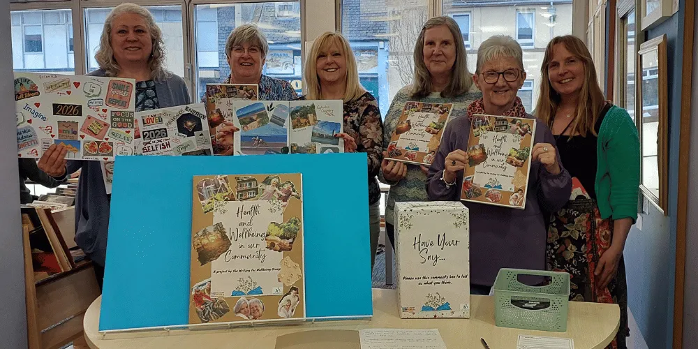 Six women standing in a row in a library holding copies of a magazine, with a sixth woman smiling