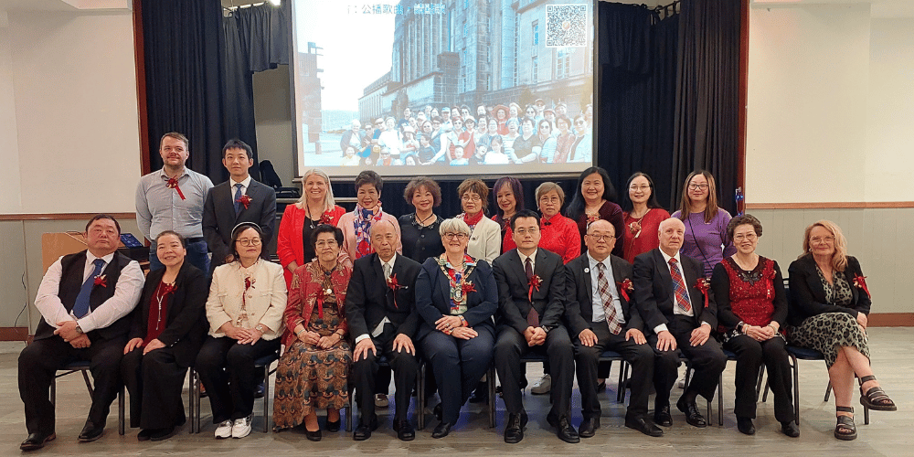 Two rows of people facing the camera smiling in front of a big screen 