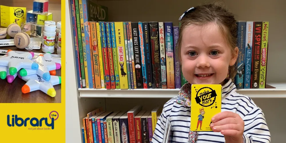 Young library reader with library card in front of bookcase and prizes in library