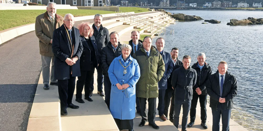 A group of men and women standing on steps, facing the camera, on a sunny day