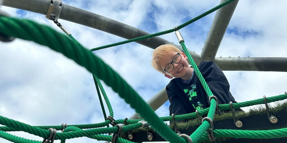 Child smiling at top of climbing frame with blue sky