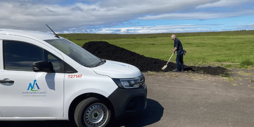 A man shovelling compost with a blue sky in the background and a small, white Council van in the foreground