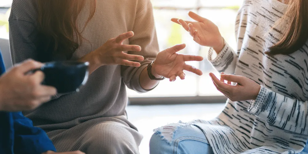 Three people talking in a group - no faces visible, only hands.