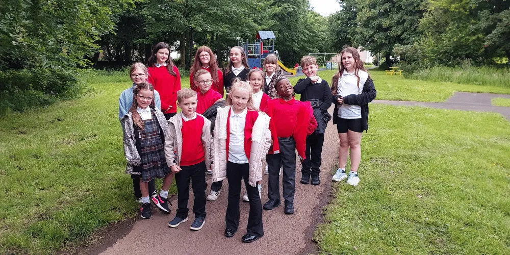Thirteen children of different ages standing smiling at the camera with a play park in the background