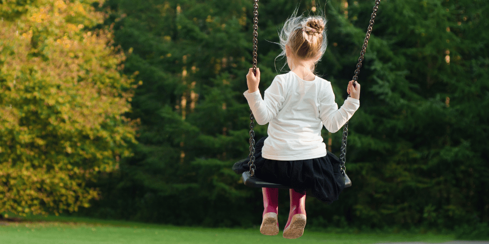 A child swinging on a swing, with her back to the camera
