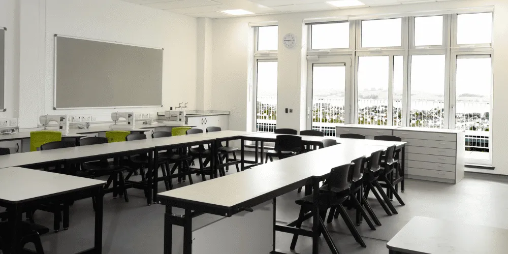 An image of a school classroom with a number of desks and chairs