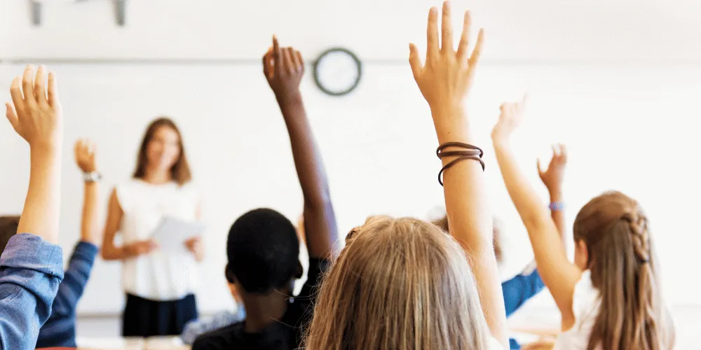 A view of school pupils answering a question from a teacher in a classroom setting