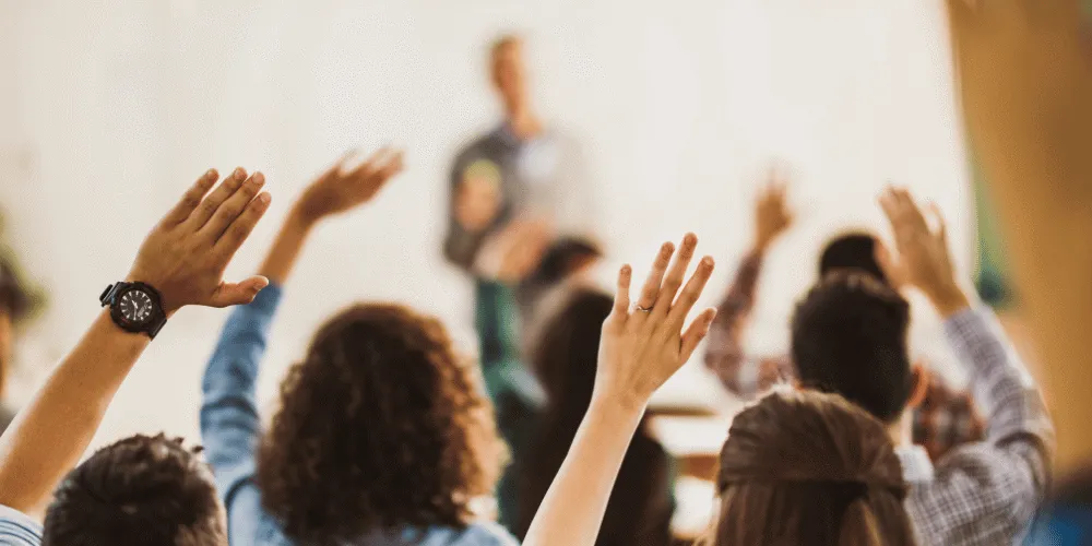 School pupils with their hands up in class to answer a question