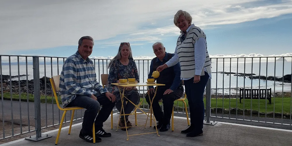 Two men and two women drinking tea with a beach in the background