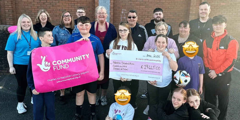 A group of mixed-age people holding up a National Lottery poster and a cheque